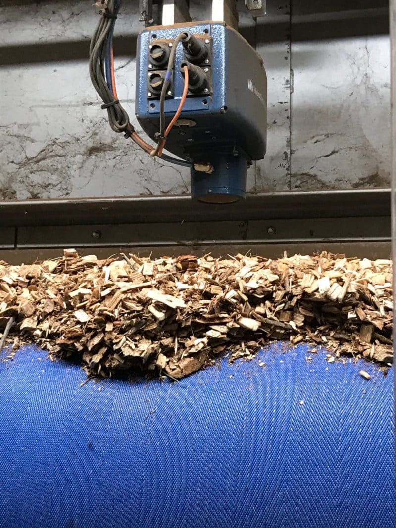 Industrial MoistTech moisture sensor mounted above a conveyor belt carrying wood chips