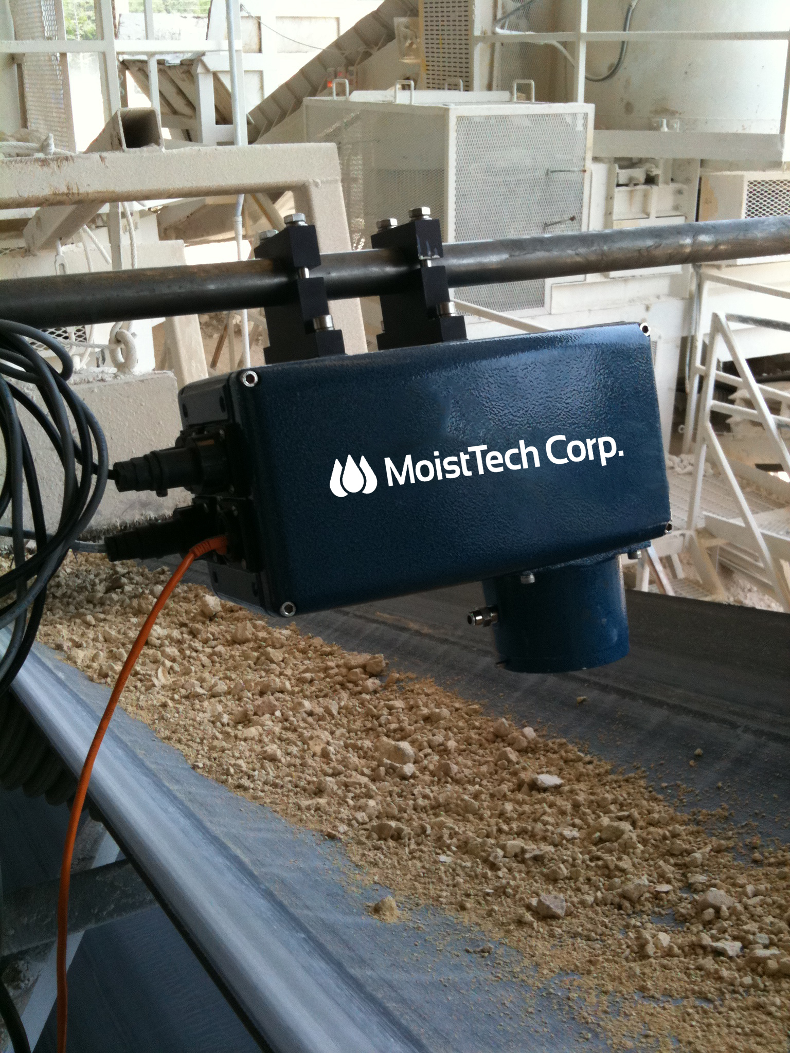 MoistTech moisture measurement device installed above bulk material on a conveyor in an industrial facility