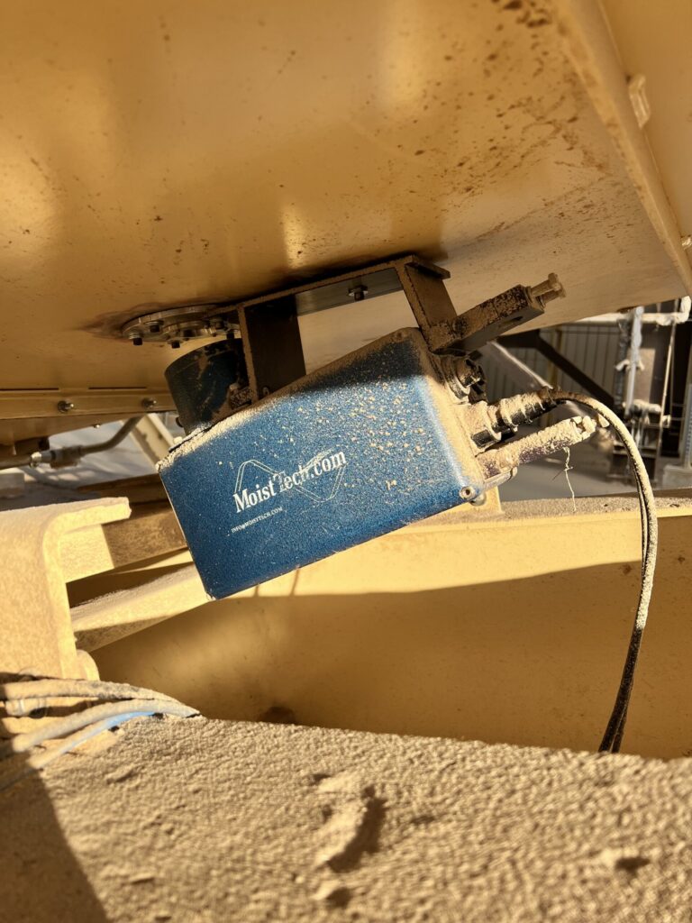 MoistTech moisture sensor with dust buildup installed beneath wood pellet processing equipment.