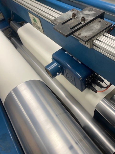 MoistTech NIR moisture sensor mounted beside a moving paper liner web on a roller converting line