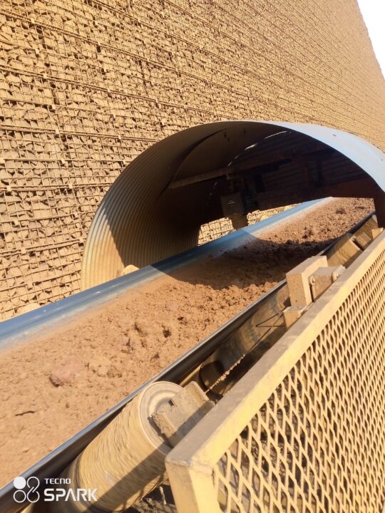 Nickel ore traveling on an industrial conveyor belt through a covered material transfer section